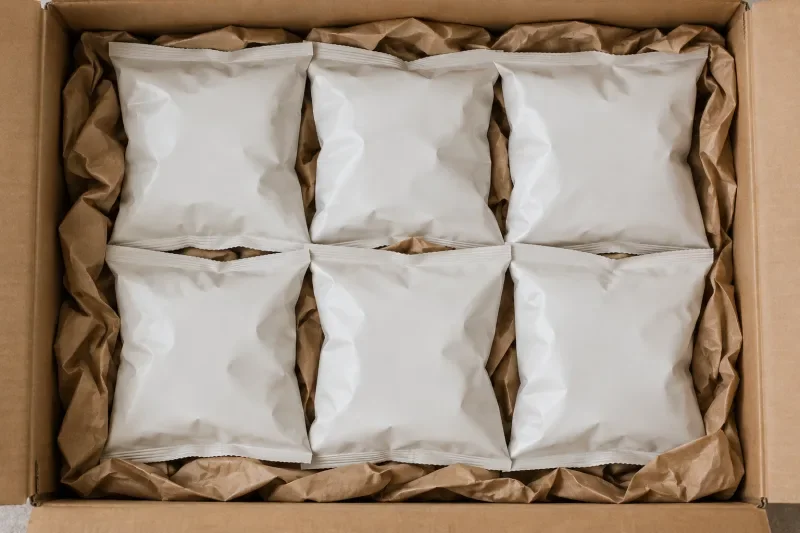 Kantong camilan polos tersusun rapi di dalam kardus dengan kertas kraft sebagai pengisi